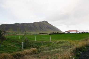 Yeşiller yemyeşil otlaklar, görkemli dağ ve İzlanda, Akranes 'te sakin bir bina.