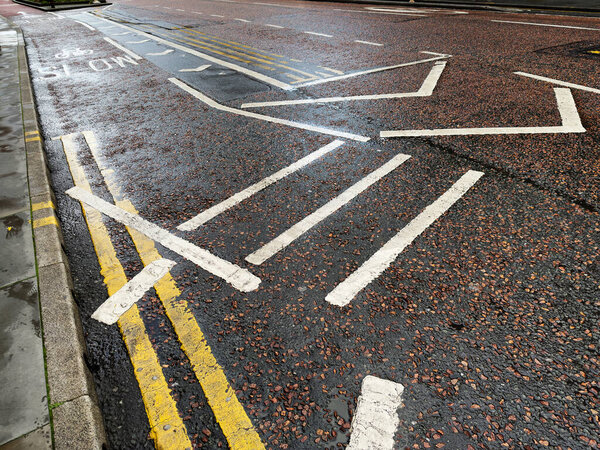 Roadway with white and yellow markings on wet asphalt in Manchester, UK.