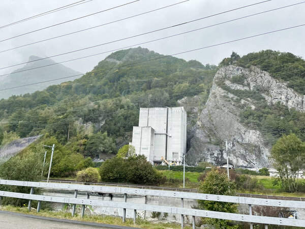Современное промышленное здание посреди скалистого ландшафта, окруженного зелеными холмами в Швейцарии