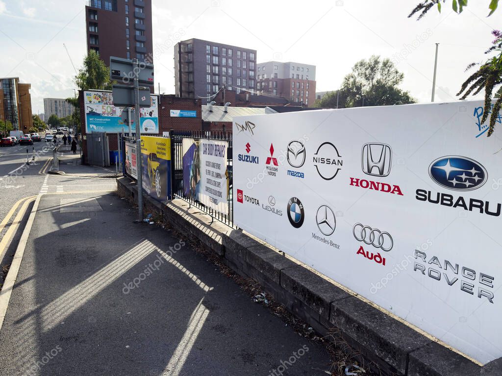 Salford, UK - September 16, 2025: Salford street scene showcasing car logos, urban buildings, and advertisements along a walkway.