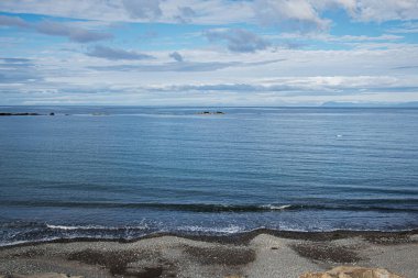 İzlanda 'da bulutlu gökyüzünün altında çakıllı plajlı sakin okyanus ve sahil manzarası
