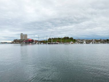 Baltimore, Maryland, ABD - 10 Nisan 2025: Baltimore, ABD 'de tekneler, binalar ve bulutlu gökyüzü ile sakin liman sahnesi.