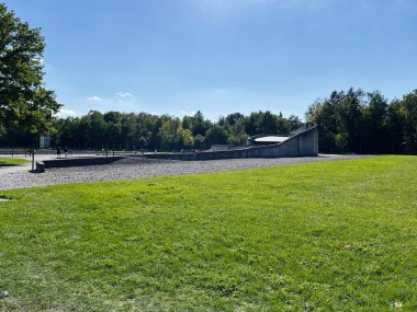 Dachau, Almanya - 29 Eylül 2022: Yeşil çimen ve ağaçlarla çevrili Dachau toplama kampındaki heykel ve patika.