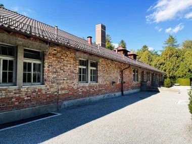Dachau, Almanya - 29 Eylül 2022: Dachau Toplama Kampındaki tuğla yapıya açık bir gökyüzü ve ağaçlar eşlik ediyor.