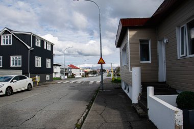 Akranes, İzlanda - 17 Eylül 2025: Akranes 'te renkli evler, park edilmiş bir araba ve bulutlu gökyüzünün yer aldığı sakin bir İzlanda caddesi.