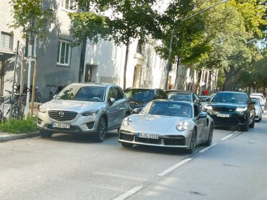 Münih, Almanya - 23 Eylül 2022: Gümüş Porsche 992 Almanya 'da güneşli bir mesken caddesinde bir sıra araba sürüyor.