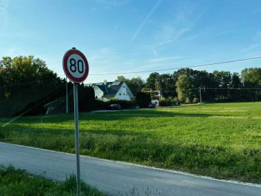 Erding, Almanya - 23 Eylül 2022: 80 hız limiti işareti, mavi gökyüzü ve temiz evler ile sessiz Alman caddesi.