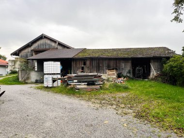 Traunreut, Almanya - 25 Eylül 2022: Almanya 'da kereste yığınları ve çakıl yolunun yanında bir su tankı ile yıpranmış ahır.