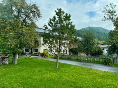 Neubeuern, Almanya - 25 Eylül 2022: Beyaz evler, yemyeşil ağaçlar ve bir dağ zeminli huzurlu Alman köyü sahnesi.