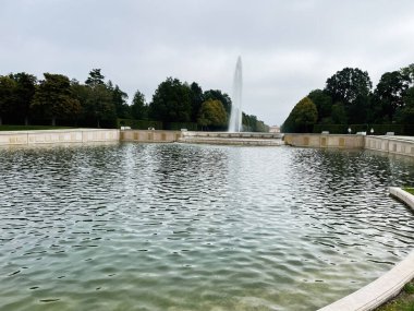 Oberschleissheim, Almanya - 25 Eylül 2022: Taş duvarlar ve bereketli ağaçlarla çevrili uzun dikdörtgen bir havuzun üzerinde büyük bir çeşme su fışkırtıyor