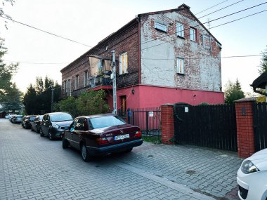 Pruszkow, Polonya - 19 Ekim 2024: Pruszkow, Polonya 'da yıpranmış tuğla bir bina ve çitin yanında park etmiş çok sayıda aracın bulunduğu sakin bir yerleşim yeri.