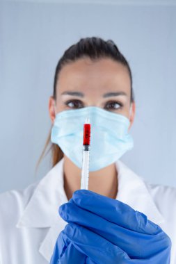 Virüs koruma maskesi ve lateks eldivenli çekici bir kadın doktor. Yanında da salyangoz iğnesi taşıyor.