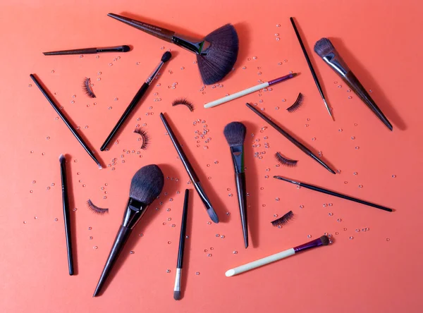 Profesyonel kullanım için farklı makyaj fırçaları ve takma kirpikleri olan turuncu yüzey