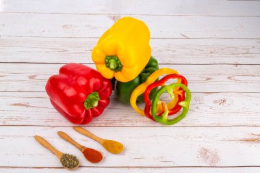 Kırmızı, yeşil, sarı biber bütün ve dilimlenmiş ve ahşap masada baharatlı üç tahta kaşık.