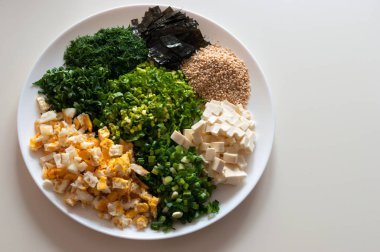 Miso çorbası için malzemeler. Kızarmış tavuk yumurta, peynir küpleri, nori, susam, soğan saplarını, ramson, maydanoz, dereotu. Plaka üzerinde.