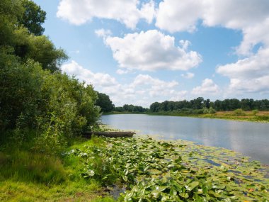 manzara: nehirde tekne, ağaçlar, bulutlar ile gökyüzü