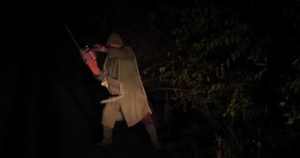 Zombie met een kettingzaag beweegt 's nachts langs de weg — Stockvideo