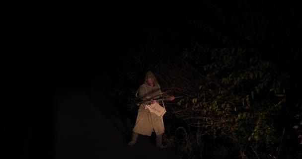 Halloween zombie med en lie och i en regnrock flyttar på natten längs vägen — Stockvideo