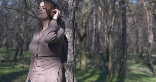 Menina bonita ouvir música em fones de ouvido e desfrutar da liberdade e beleza da natureza na floresta . — Vídeo de Stock