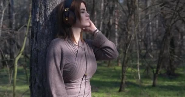 Piękna młoda dziewczyna słuchając muzyki na słuchawkach i ciesząc się swobodą i pięknem natury w lesie. — Wideo stockowe