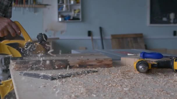 Un carpintero trabaja con una cepilladora eléctrica en su taller de carpintería. Imágenes en cámara lenta con marco de luz natural. — Vídeos de Stock