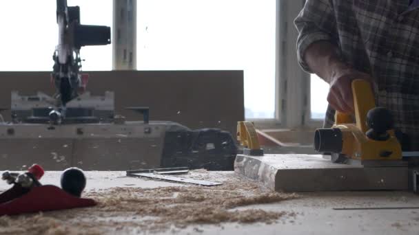 Un falegname lavora con una pialla elettrica nella sua falegnameria. Filmati al rallentatore con cornice a luce naturale. — Video Stock