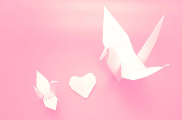 白色折纸起重机和心脏之间 鸟纸在粉红色背景 概念情人节 — 图库照片