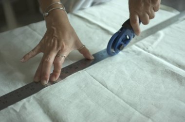 Atölyede kesici ile profesyonel terzi kesme beyaz kumaş, closeup