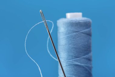 Büyük gümüş iğne dikiş iplik ile için. Dikey olarak bobin mavi iş parçacığı ayakta. Mavi arka plan, kopya alanı.