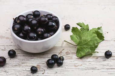 Taze Olgun siyah kuş üzümü rustik ahşap zemin üzerinde. Kase ile yıpranmış gri ahşap masa üzerinde yeşil yaprakları ile doğal organik çilek, kopya alanı ile yeni berry hasat üstten görünüm