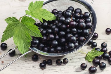 Kevgir ile taze siyah frenk üzümü ve orijinal ahşap arka plan üzerinde bırakır. Sağlıklı gıda, berry tatlı. Tasarım, kopya alanı için yer.