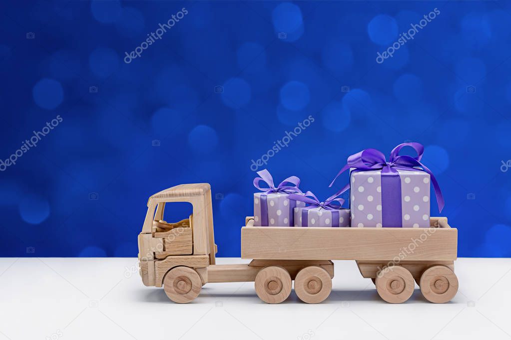 Gift boxes in violet and white polka-dot paper, carrying wooden toy truck. Copy space. Winter background.