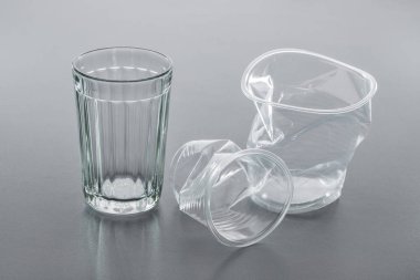 Basit cam ve plastik bardakta buruşuk gri arka plan, yakın çekim. Geri dönüşüm kavramı.