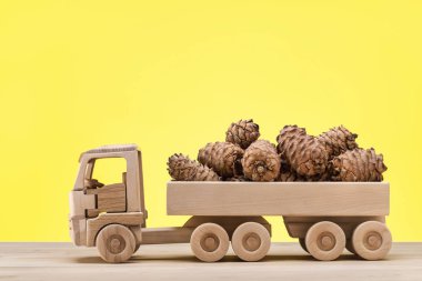  Ahşap oyuncak araba arka sedir konileri taşır. Yakın çekim, sarı arka plan.