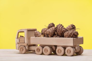 Ahşap oyuncak araba arka sedir konileri taşır. Yakın çekim, sarı arka plan.