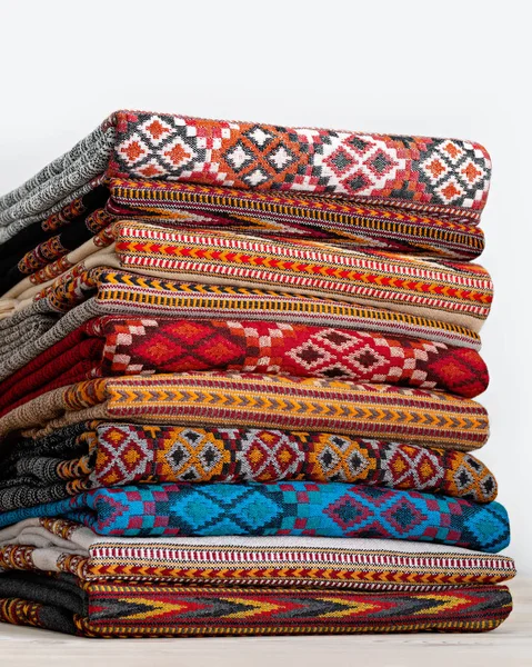 Woolen blankets, stoles folded and stacked in stack of several rows. Beautiful texture and colors of products create amazing effects. Studio shot.