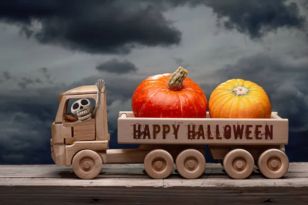 Cadılar Bayramınız kutlu olsun, portakal kabakları ve kuru akçaağaç yaprakları insan iskeleti olan tahta oyuncak kamyonda. Kasvetli bulutlarla akşam gökyüzü. Tahta yüzey, stüdyo çekimi..