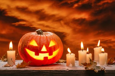  Cadılar Bayramı 'nın ışıltılı balkabağı, sonbahar yaprakları ve ahşap arka planda yanan mumlar. Kıpkırmızı, uğursuz bulutlu bir gökyüzü.