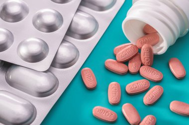 Tabletler gümüş su topladı. Pembe haplarla dolu beyaz bir kavanoz. İlaç sanayisi. Mavi arkaplan, stüdyo çekimi.