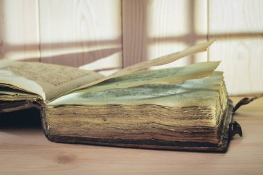 Tahta masanın üzerinde sarı sayfalar olan çok eski, açık bir kitap. Arkaplanda ışık ve gölge.