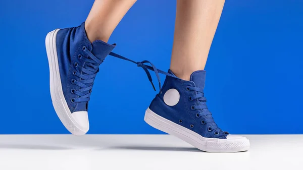 A pair of blue gym shoes with laces on women\'s legs.
