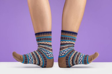 Kadınların ayaklarında süslemeli sıcak örülmüş çoraplar vardır. Leylak arkaplan, stüdyo çekimi.