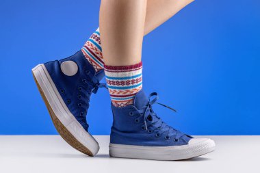  Mavi spor ayakkabılı, rahat çoraplı, mavi arka planlı kadın bacakları. Rahatlama ve rahatlama kavramı.