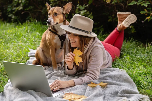 Smiling lady with  laptop and  dog for  walk in the autumn park.