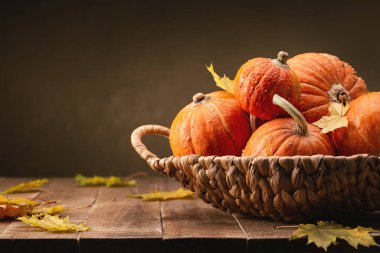 Hasır sepetin içinde turuncu yuvarlak balkabakları ve koyu ahşap masada kuru yapraklar. Mutlu Cadılar Bayramı.