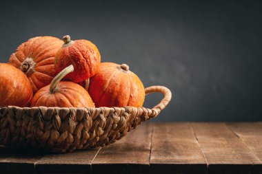 Hasır sepetin içinde koyu ahşap masada turuncu yuvarlak balkabakları. Uzayı kopyala Mutlu Cadılar Bayramı.