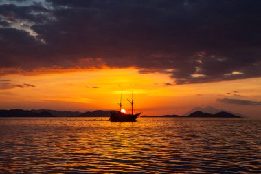 A Pinisi schooner sails through calm seas at sunset in Komodo National Park, Indonesia. This tropical region is a popular destination for scuba divers, snorkelers, and nature lovers. clipart