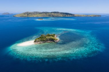 Seen from a bird's eye view, an idyllic island is surrounded by a healthy coral reef in Komodo National Park, Indonesia. This tropical area is known for its marine biodiversity as well as its dragons. clipart