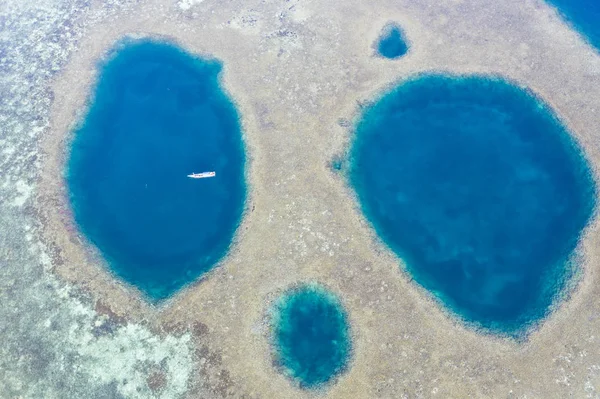 Blue holes are found amid a shallow reef flat on the island of Sebayor in Komodo National Park, Indonesia. These blue holes originally formed as limestone sink holes when sea levels were lower.