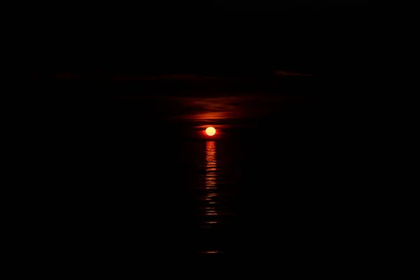 The sun sets over a dark ocean.